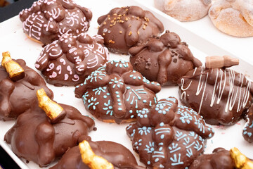 A tray of assorted chocolate donuts with various designs and colors. The donuts are arranged in rows. Day of the Dead celebration in Mexico, papel picado crafts, offerings, La Catrina