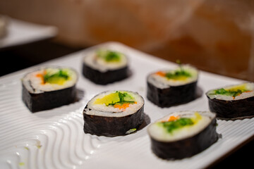 Close up of cucumber sushi rolls with seaweed wrap on white plate.