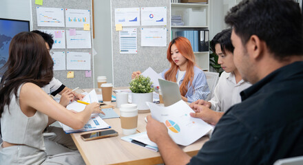 Asian business startup team members convene in a modern coworking office. They are engaged in design planning, sharing ideas, and brainstorming concepts to propel their startup forward.