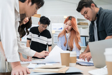 Asian business startup team members convene in a modern coworking office. They are engaged in design planning, sharing ideas, and brainstorming concepts to propel their startup forward.