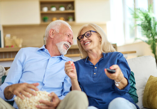 Portrait of an elderly senior happy couple watching tv together eating popcorn at home