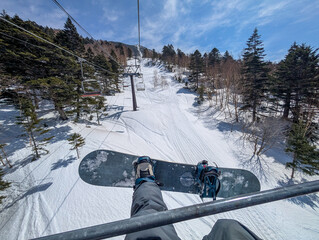 First person view of a snowboarder riding a chairlift up a snowy mountain in Japan.
