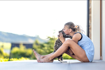 Young cheerful smiling girl playing with domestic kitten. Woman on farm rejoicing at birth of pet. Child playing with cat in yard of family house or park