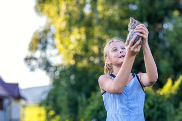 Young cheerful smiling girl playing with domestic kitten. Woman on farm rejoicing at birth of pet. Child playing with cat in yard of family house or park
