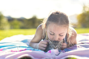 Young cheerful smiling girl playing with domestic kitten. Woman on farm rejoicing at birth of pet. Child playing with cat in yard of family house or park
