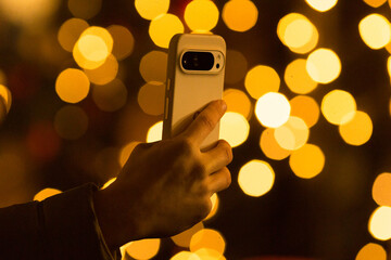 Close-up of a hand holding a smartphone while filming a festive event. Modern lifestyle and digital...