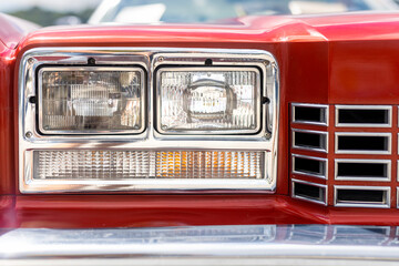 Detail of the red front hood with the light of an American retro car. Mask of an classic old hystory veteran