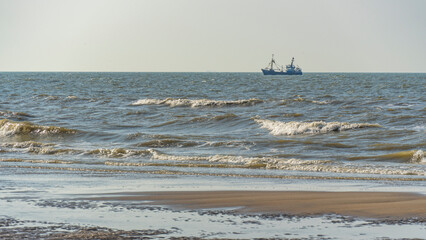 single ship is sailing on the North Sea, ship, sails and waves shine in the evening light, North Sea beach before sunset with waves of the ocean
