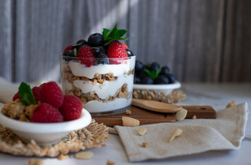 Yogurt parfait with granola, raspberries, and blueberries on a rustic background. A healthy and delicious breakfast or snack idea.