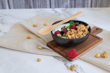 Healthy breakfast bowl with granola, yogurt, raspberries, blueberries, and mint on a linen napkin. 