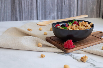 Healthy breakfast bowl with granola, yogurt, raspberries, blueberries, and mint on a linen napkin. 