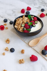 Healthy breakfast bowl with granola, yogurt, raspberries, blueberries, and mint on a linen napkin. 