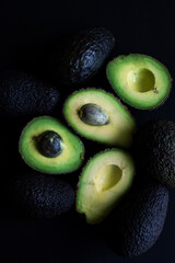 Fresh whole and cut avocados on a dark background. Healthy vegan food, rich in nutrients and healthy fats.
