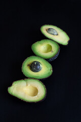 Sliced avocados arranged in a row on a dark background, showcasing their bright green interior.