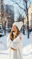 Happy smiling woman in cozy white winter fashion. Young person wearing a knit sweater and hat in a snowy city park