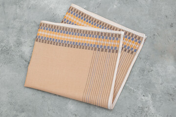 A neatly folded men's handkerchief with a beige base and a patterned band of woven stripes rests on a textured gray background.
