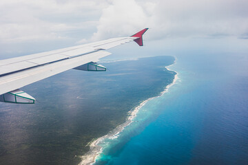 Airplane view of a beautiful coastline with turquoise waters and green land beneath a cloudy sky