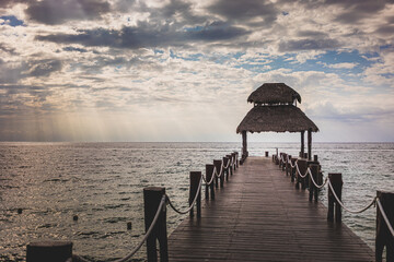 Serene pier extending into tranquil waters under a cloudy sky at sunset in a coastal location