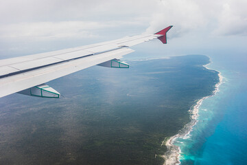 View of a tropical coastline from a plane window during a scenic flight over a lush forested area