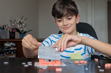 Fototapeta premium young boy at home builds a miniature house from toy ceramic bricks, focusing on construction and creativity. logic, fine motor skills, and concentration. autism support, ADHD therapy, screen free 