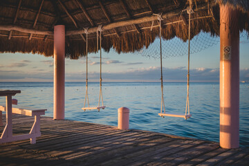 Relaxing swings on a beachside pier at sunset overlooking calm waters and a peaceful sky