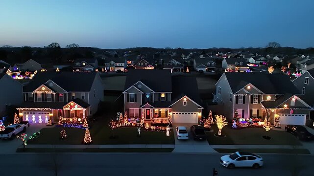 Aerial drone captures quiet suburban neighborhood at dusk, showcasing houses adorned with elaborate, competing Christmas light displays.