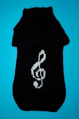 on a blue background lies a knitted black sweater pets for dogs with a white treble clef pattern. top view. handmade