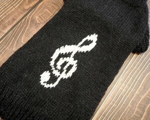 On a wooden background lies a knitted black sweater to dogs pets with a white treble clef pattern. side view. handmade