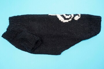 on a blue background lies a knitted black sweater pets for dogs with a white pattern of a treble clef, on the side. handmade