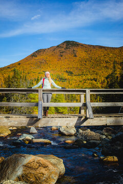 Woman enjoys a scenic autumn view on bridge over stream in the mountains