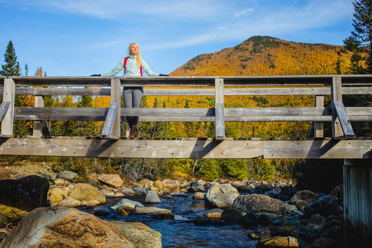 Woman enjoys nature on a wooden bridge over a clear stream surrounded by autumn colors in the mountains