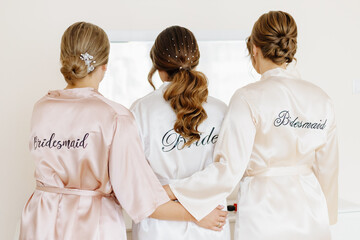 Bride in a satin robe with the inscription “Bride” on the back, preparing for her wedding day....