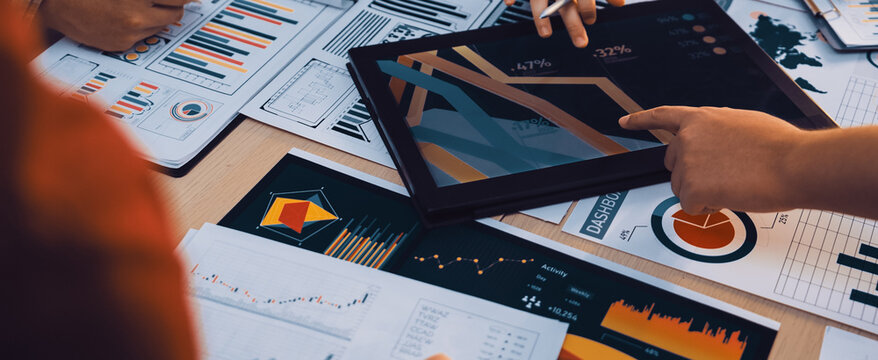 A diverse business team engages in collaborative work, analyzing charts and reports while using a digital tablet to drive strategic decisions in a modern office setting. SACTR