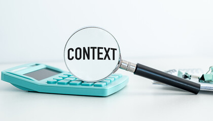 A calculator sits on a table next to a magnifying glass. The magnifying glass is focused on the word CONTEXT, which is written on the calculator