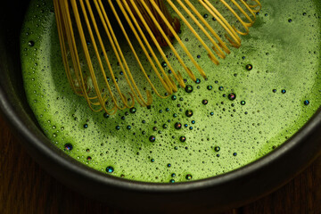 Ceremonial Matcha Preparation. A bamboo whisk stirs vibrant green matcha with bubbles.