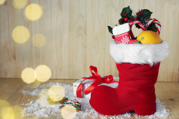 Obraz premium Saint Nicholas day tradition. Red boot with sweets, festive decor, gift box and artificial snow on wooden table