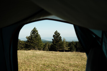 View from inside a tent looking out at the scenic Divcibare landscape in Serbia. Camping and outdoor adventure concept with mountains and trees