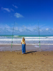 A lonely woman contemplates the sea between two fishing rods, on a beautiful day of sun and sea