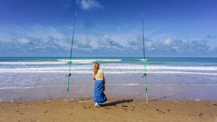 A lonely woman contemplates the sea between two fishing rods, on a beautiful day of sun and sea