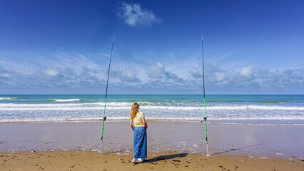 A lonely woman contemplates the sea between two fishing rods, on a beautiful day of sun and sea
