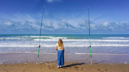A lonely woman contemplates the sea between two fishing rods, on a beautiful day of sun and sea
