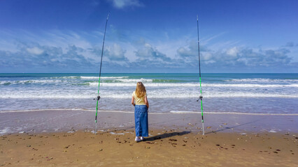 A lonely woman contemplates the sea between two fishing rods, on a beautiful day of sun and sea