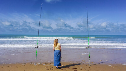 A lonely woman contemplates the sea between two fishing rods, on a beautiful day of sun and sea