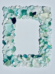 Rectangular frame made of sea glass pieces in aqua, turquoise, and white on light background. Natural coastal decoration, eco-friendly design, ideal for text or creative layouts.