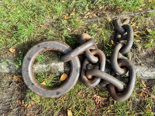 Old rusty iron chain with a large circular ring lying on grass, symbol of strength, history, and industrial heritage.