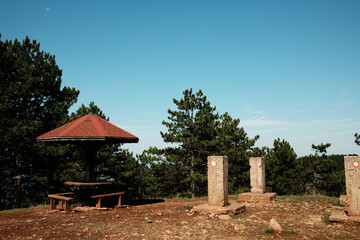 Mountain picnic shelter and stone markers at a viewpoint in Divcibare, Serbia. Clear sky and pine forest background