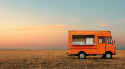 An orange food truck parked in an open field during sunset, showcasing a serene landscape with soft colors in the sky.