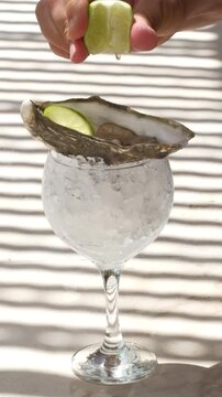 close-up shot captures a hot summer as a hand squeezes a lime over a chilled oyster on a glass with ice. Sunlight highlights splash of juice, evoking feelings of a seaside holiday cooling experience