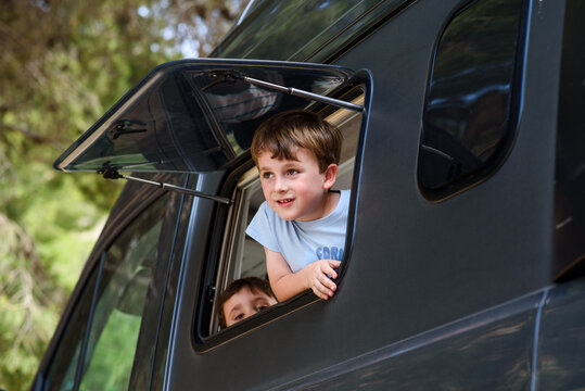 Children looking out of camper van window enjoying road trip