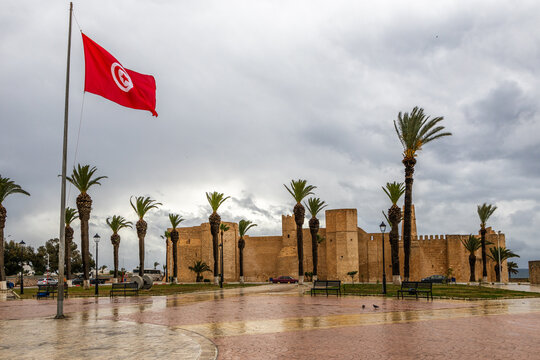 Tunisian national flag with lots of palms and Ribat of Monastir under cloudy skies, Monastir, Monastir Governorate, Tunisia